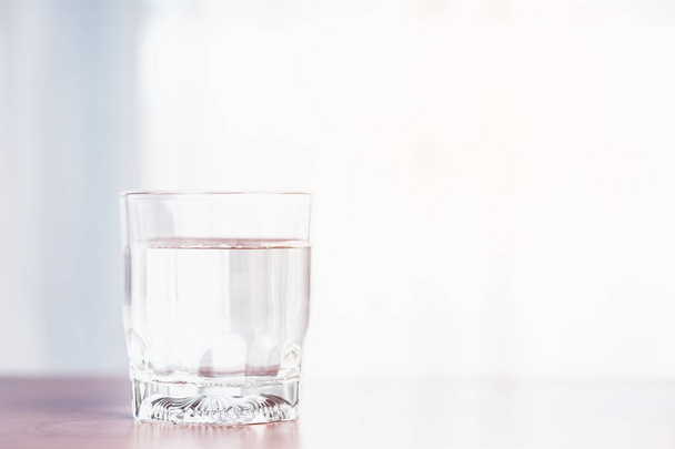 Ein klares Glas mit Wasser steht auf einem Holztisch mit sanftem orangefarbenem Sonnenlicht von außen für das Konzept eines gesunden Wasserverbrauchs.. - Foto, Bild