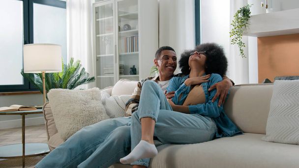 Smiling laughing carefree African American happy family couple married woman girl man guy boyfriend and girlfriend domestic dating bonding conversation laugh funny love affection talking at home couch - Photo, Image
