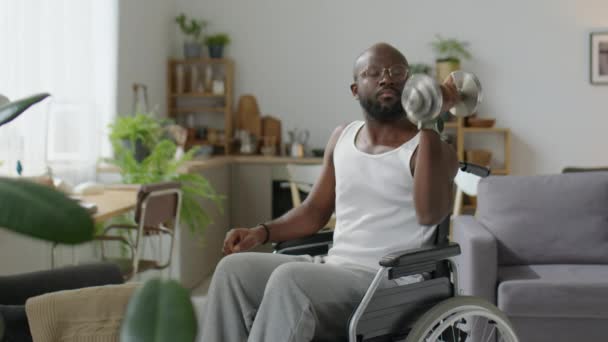 Hombre negro con discapacidad sentado en silla de ruedas y haciendo mancuerna sentada un brazo hombro prensa mientras tiene entrenamiento en casa - Metraje, vídeo