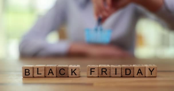 Woman hand puts toy shopping basket on phrase from wooden cubes Black Friday. Concept of shopping day with big discounts in stores slow motion - Footage, Video