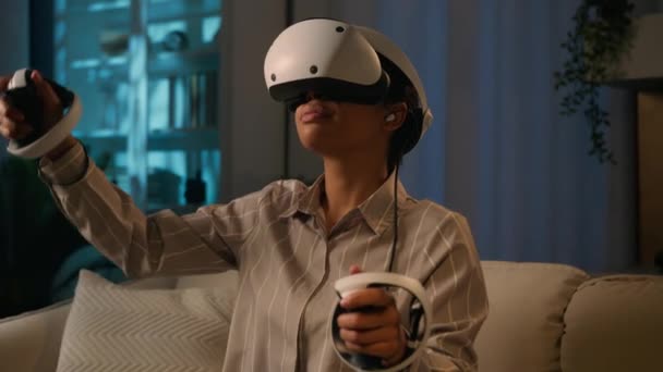 Mujer afroamericana en casco VR gafas de realidad aumentada metaverse juego simulación explorar mundo 3D jugar video juego modernas tecnologías virtuales cyber jugar con controladores en casa de noche - Imágenes, Vídeo