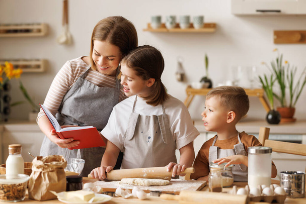 Junge lächelnde Mutter backt Teigkekse mit süßen Kindern: Sohn und Tochter stehen gemeinsam in der heimischen Küche,   - Foto, Bild
