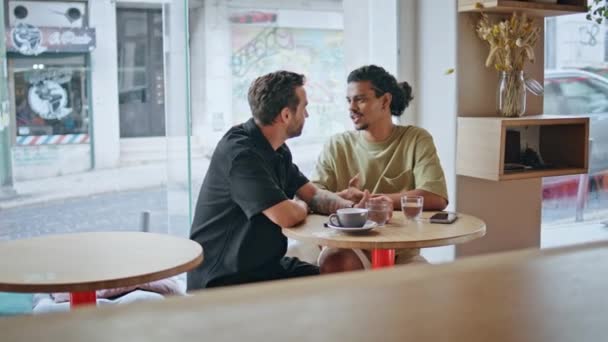 Kaksi homomiestä flirttailee romanttisessa tapaamisessa modernissa kahvilassa. Pari homoseksuaalista kumppania puhumassa hymyillen kahvilassa nauttien romantiikasta. Huoleton onnellinen monirotuinen ystäville viettää viikonlopun yhdessä. - Materiaali, video