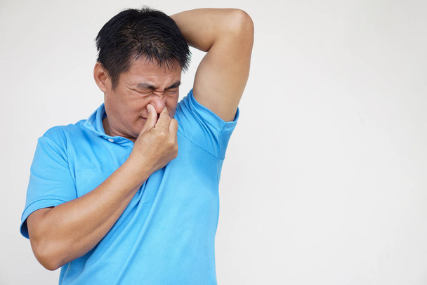 Asian man is checking his odor underarm, close his nose with hand, feel disgusted the body strong smell. Concept , health problem. Unpleasant body odor , smell nasty reaction. Negative emotion.        - Photo, Image