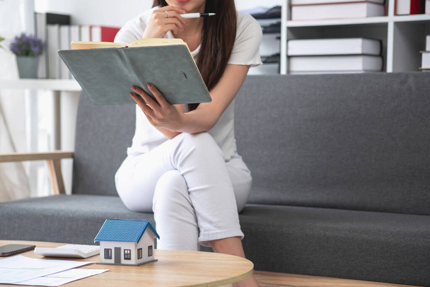 woman sitting on cozy sofa and planning and calculate expense and mortgage with calculator and home on desk, insurance and budget of residential, loan and residence, business and property concept. - Photo, Image