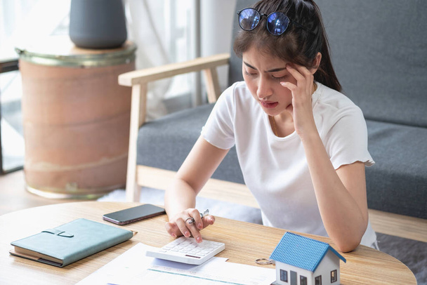 Молодая азиатка, сидящая и рассчитывающая расходы и ипотеку с калькулятором и домом на столе. - Фото, изображение