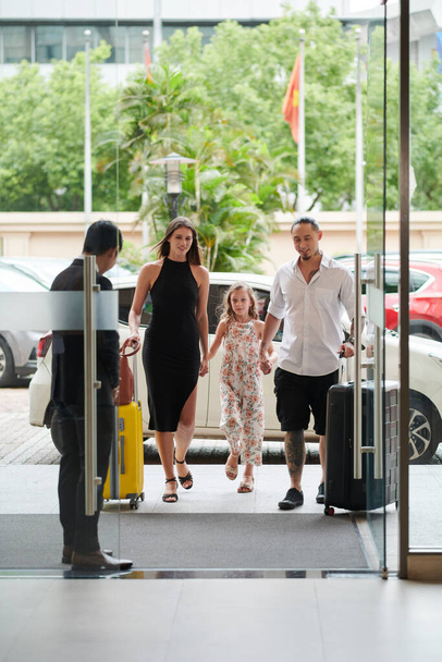 Neşeli anne, baba ve küçük kız otel salonuna giriyor. - Fotoğraf, Görsel