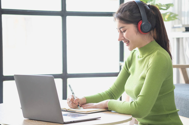 Ázsiai nő egy gyönyörű arc egy zöld hosszú ujjú ing ül, és pihentető néz filmeket Zenét hallgatni egy laptop, mobiltelefon, és fejhallgató boldogan belül nappali otthon. - Fotó, kép