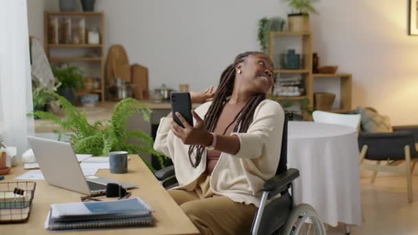 Medium long shot di donna afroamericana in sedia a rotelle sorridente e in posa per fotocamera smartphone con il piccolo figlio mentre si scattano selfie insieme a casa - Filmati, video