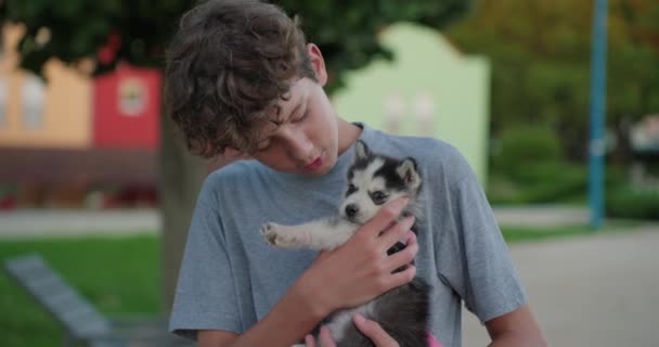 Un adolescente sostiene a un pequeño cachorro en sus brazos disfrutando del momento y abrazándolo. - Imágenes, Vídeo