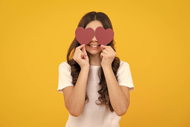 Tinédzser lány tartja formás szív, szív alakú jel. Gyermek kezében egy piros szív szerelem ünnep Valentin szimbólum, elszigetelt sárga alapon. Boldog tinédzser, pozitív és mosolygós érzelmek tini lány - Fotó, kép