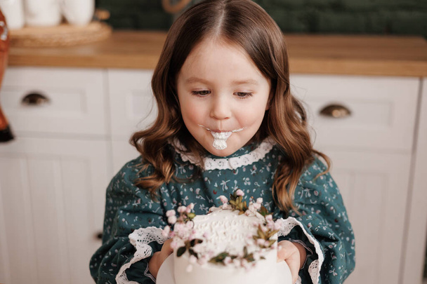 可愛い小さな子供の女の子はお祝いのドレスを身に着けている誕生日パーティーで装飾された花名ケーキから一口を取ります。. - 写真・画像