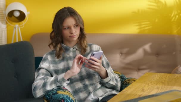 Στοχαστική γυναίκα που χρησιμοποιεί smartphone στο σπίτι. Έξυπνο κορίτσι πληκτρολογεί μήνυμα στο κινητό. Αμφιβολικός μαθητής που σκέφτεται τις εξετάσεις. Κουρασμένη κυρία κάθεται στο τραπέζι με το κινητό τηλέφωνο. Έννοια σύνδεσης, 4k πλάνα - Πλάνα, βίντεο