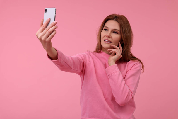 Beautiful woman taking selfie on pink background - 写真・画像