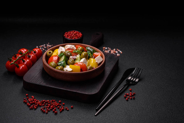 Πεντανόστιμη φρέσκια, ζουμερή ελληνική σαλάτα με φέτα, ελιές, ντομάτες, αγγούρι, πιπέρι, αλάτι και μπαχαρικά σε σκούρο μπετόν φόντο - Φωτογραφία, εικόνα