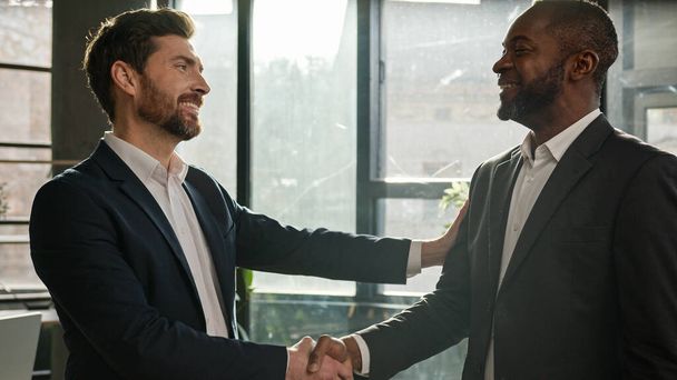 Caucasian boss hr manager man shake hand of African American candidate partner client making deal hiring thanking for collaboration congratulation. Diverse business partners men in office handshaking - Foto, immagini