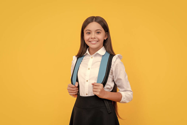 childhood happiness. child with school bag. happy teen girl carry backpack. back to school. knowledge day. concept of education. kid with long hair in uniform on yellow background. september 1. - Photo, Image