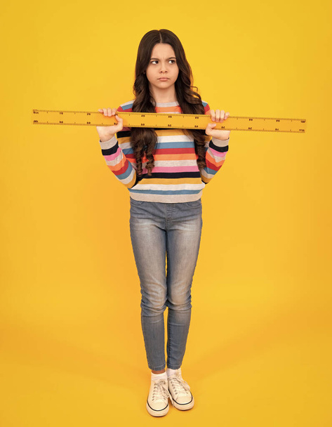 Back to school. School girl hold ruler measuring isolated on yellow background. Unhappy sad teenager girl - Foto, imagen