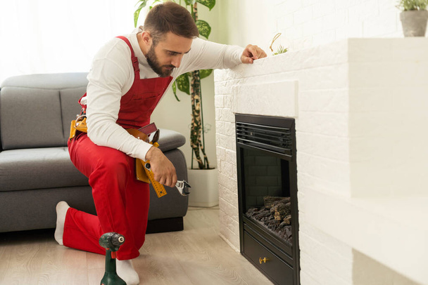 Professional technician sealing electric fireplace near white wall in room. - Foto, Imagem