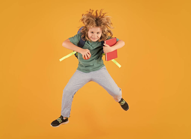 Full length of excited kid jumping. School boy in school uniform with backpack jumping on yellow isolated background. Kids learning knowledge and kids education concept - Foto, imagen