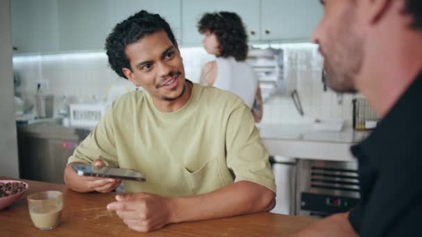 Men exchange phone numbers after acquaintance in modern cafeteria close up. Two multiracial guys talking at friendly meeting in small cafe. Latino mustache male hipster smiling looking on new friend. - Footage, Video