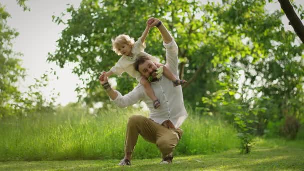 Egy boldog apa sétál egy aranyos kisfiúval a vállán ülve. A család együtt tölti az idejét a mezőn. - Felvétel, videó