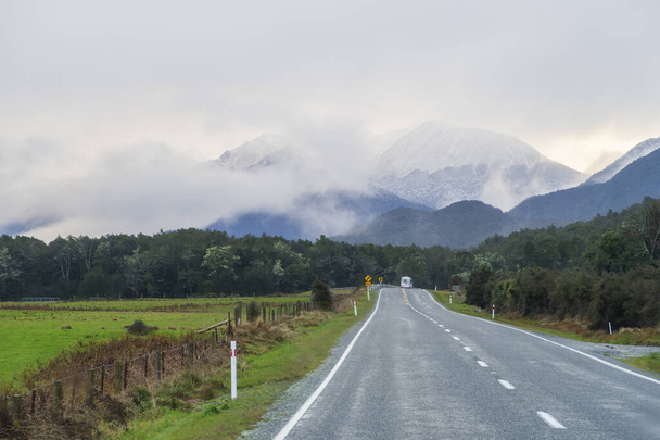 Fotografia di un furgone con i turisti che guidano su una strada verso una catena montuosa coperta di neve e nebbia nel Fiordland National Park sull'isola meridionale della Nuova Zelanda - Foto, immagini