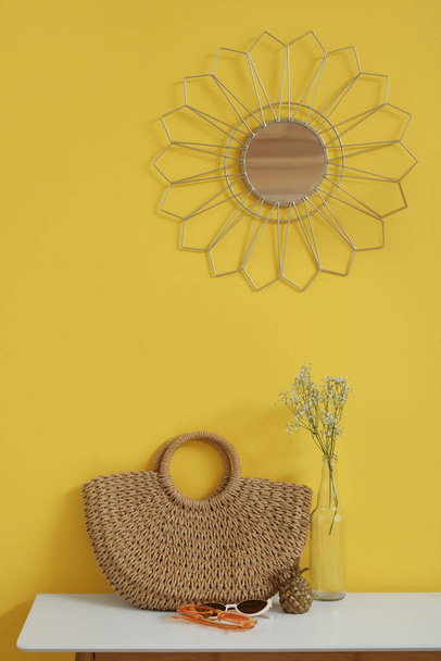 Интерьер стильного коридора с зеркалом, плетеной сумкой и вазой на консольном столе - Фото, изображение