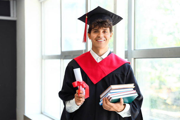 Hombre estudiante de posgrado con diploma y libros cerca de la ventana en la habitación - Foto, Imagen