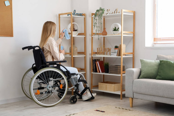 Młoda kobieta na wózku inwalidzkim sprzątanie półki w domu - Zdjęcie, obraz