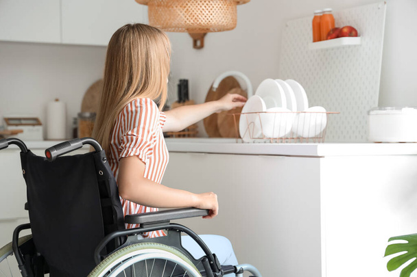 Young woman in wheelchair taking dish at home - Valokuva, kuva