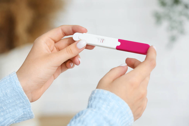 Θηλυκά χέρια με θετικό τεστ εγκυμοσύνης σε θολή φόντο, κοντινό πλάνο - Φωτογραφία, εικόνα