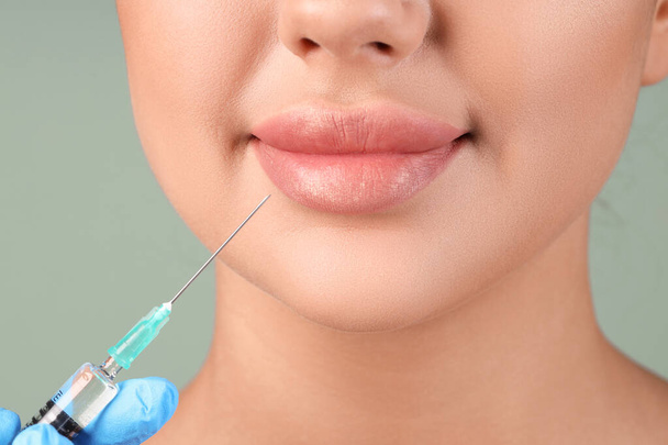 Young woman receiving lip injection on green background, closeup - Photo, Image