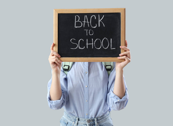 Школярка в рюкзаку тримає дошку з текстом BACK To SCHOOL на сірому фоні - Фото, зображення
