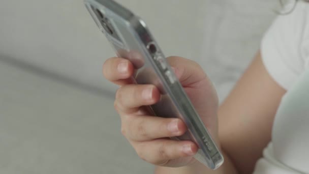 Close-up tiro da mão da mulher asiática usando o telefone móvel para fazer compras, jogar jogos, conversando em mídias sociais sentado no sofá em casa. Conceito de uso de smartphone, vício em celular, tempo de relaxamento em casa - Filmagem, Vídeo