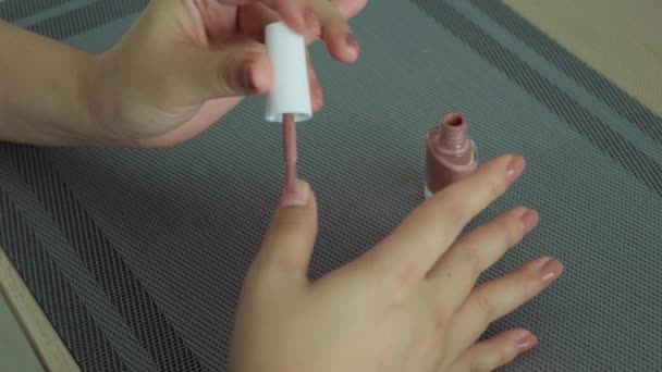 Γυναικεία χέρια με βερνίκι νυχιών στο τραπέζι στο σπίτι, στιγμή χαλάρωσης, αυτο-βάψιμο νυχιών - Πλάνα, βίντεο