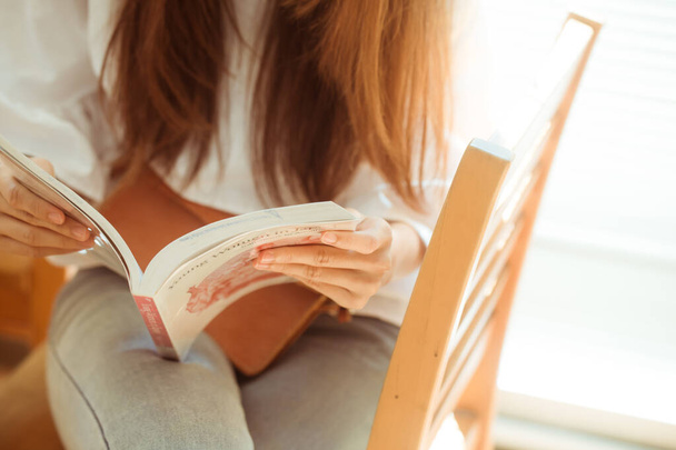 Γυναίκα κάθεται σε καρέκλα ξύλο κρατώντας το βιβλίο για να διαβάσει στην βιβλιοθήκη, επιχειρηματική ιδέα εκπαίδευσης. - Φωτογραφία, εικόνα