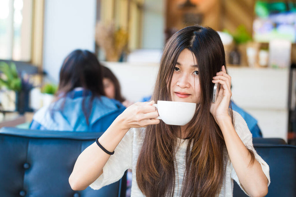 Ασιατικός επιχειρησιακός φοιτητής κάθεται στο καφενείο και να μιλάμε για smartphone με φλιτζάνι καφέ - Φωτογραφία, εικόνα