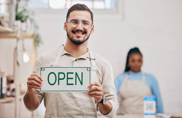 Open, sign and man with small business or restaurant happy for service in a coffee shop, cafe or store with a board. Smile, manager and portrait of an entrepreneur ready for operations with billboard. - Photo, Image