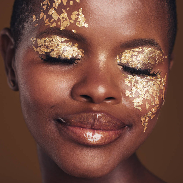 Золотая, креативная и черная женщина с макияжем для эстетики красоты, изолированная в студии на коричневом фоне с закрытыми глазами. Искусство, роскошь и лицо африканца с косметическим гламуром или дизайном для шкур. - Фото, изображение