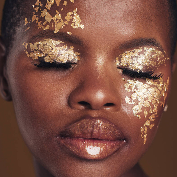 Gold, art and black woman with makeup for beauty aesthetics isolated in a studio brown background eyes closed. Creative, luxury and face of African person with cosmetic glamour or design for skincare. - Photo, Image