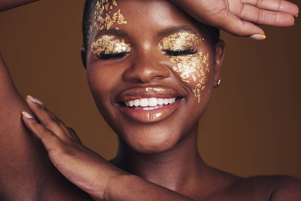 Золото, творчість і мистецтво на обличчі чорної жінки з макіяжем для краси естетики ізольовані на студійному коричневому фоні. Посмішка, розкіш і щаслива людина з косметичним гламуром або дизайном для скінарію. - Фото, зображення