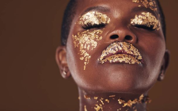 Stüdyonun kahverengi arka planında izole edilmiş güzellik estetiği makyajlı Afrikalı bir kadının altın, sanat ve yüzü. Yaratıcı, lüks ve cilt bakımı için kozmetik cazibesi ya da tasarımı olan kişi. - Fotoğraf, Görsel