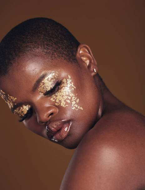 Мистецтво, блиск і чорна жінка з золотим макіяжем на коричневому тлі, фарбою для обличчя та косметикою. Сяйво, сяйво та африканська модель в студії за красу, моду та естетичну свободу в розкішних скінареях - Фото, зображення
