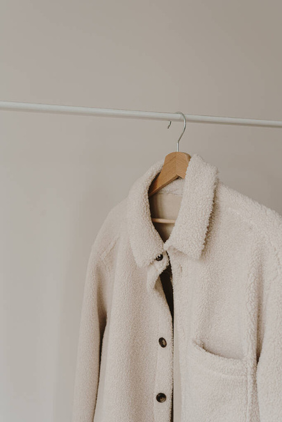 Herfst bovenkleding op hanger over witte muur. Warm wit jasje. Esthetische garderobe met kleding in neutrale kleuren - Foto, afbeelding