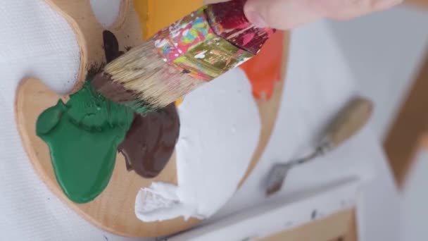 The hand of a young artist mixes paints on a palette that stands on the table. Basic colors. Work with a thick paintbrush. Workplace of the artist - Séquence, vidéo
