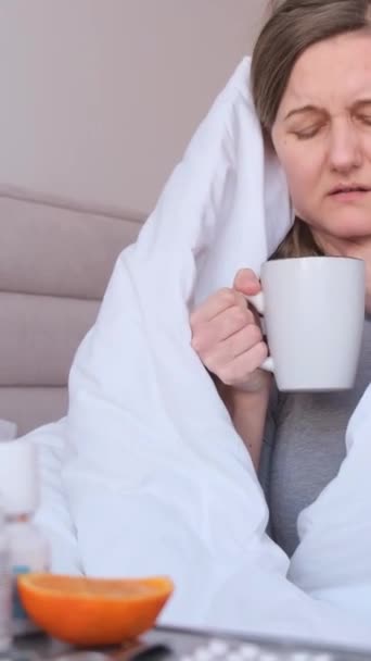Πορτρέτο μιας νεαρής γυναίκας που έχει SARS και πίνει ζεστό τσάι. Απομόνωση στο σπίτι. Αυτοθεραπεία κρυολογημάτων. Κάθετη βίντεο - Πλάνα, βίντεο