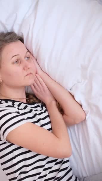 Μια θλιμμένη, αναστατωμένη γυναίκα ξαπλώνει στο κρεβάτι και αποκοιμιέται. Κουρασμένη γυναίκα. Κάθετη βίντεο - Πλάνα, βίντεο