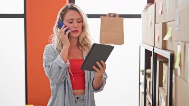 Mujer rubia joven comercio electrónico trabajador de negocios que habla en el teléfono inteligente mediante la comprobación de touchpad en la oficina - Imágenes, Vídeo