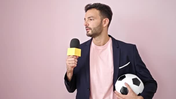 Joven reportero de fútbol hispano haciendo entrevista hablando sobre aislado fondo rosa - Imágenes, Vídeo